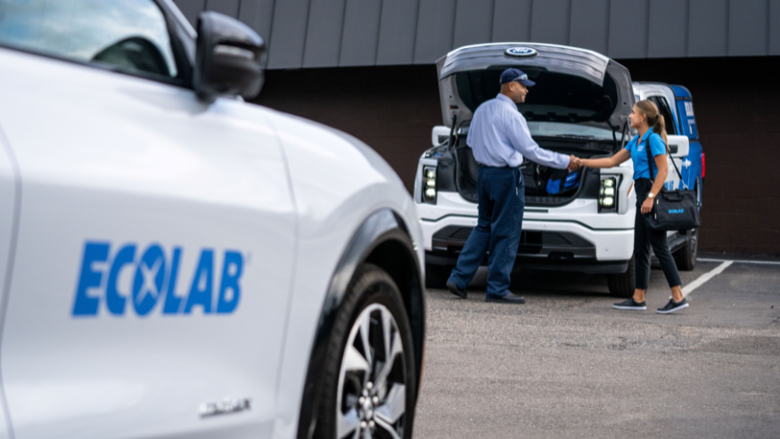 Ford and Ecolab associates shaking hands. Ecolab vehicles, Ford brand, in the front and in the background. . 